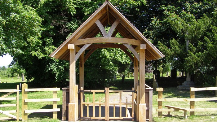 Wooden gate with triangular roof, surrounded by trees and grass