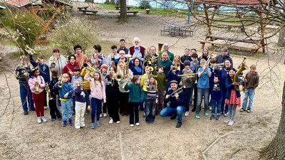 Eine große Gruppe von Menschen, darunter Kinder und Erwachsene, die sich gemeinsam im Freien in einer parkähnlichen Umgebung fotografieren lassen.