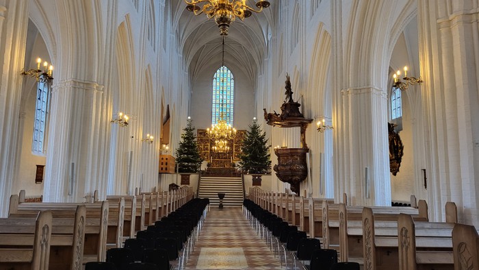 Indre del af en stor, belyset kirke med høje buevægge og træbænke.