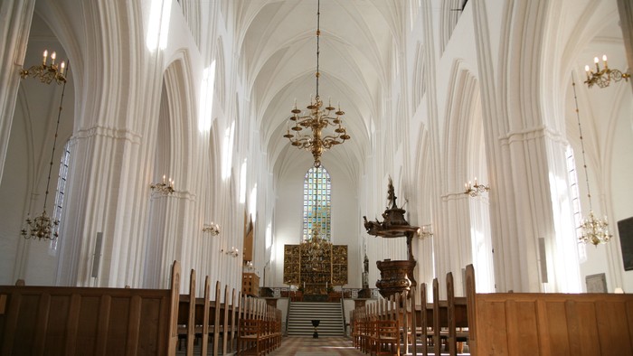 Indre del af en stor, belyset kirke med høje buegange og træbænke.