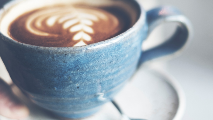 Nahaufnahme eines Latte-Art-Kaffees in einer Keramiktasse auf einer Untertasse mit einem Löffel.