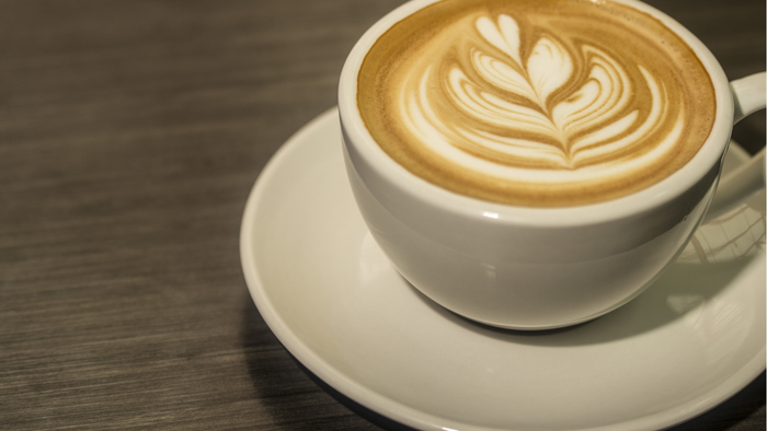 Ein wunderschön mit Latte-Art verzierter Kaffee mit einem floralen Muster steht auf einer Untertasse.