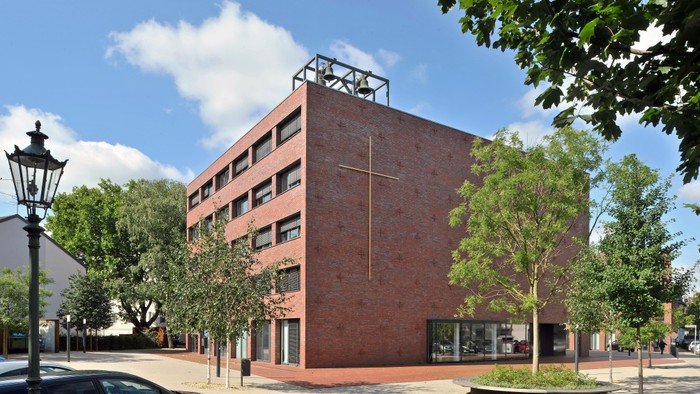 Modernes Kirchengebäude mit Kreuz und Bäumen im Vordergrund