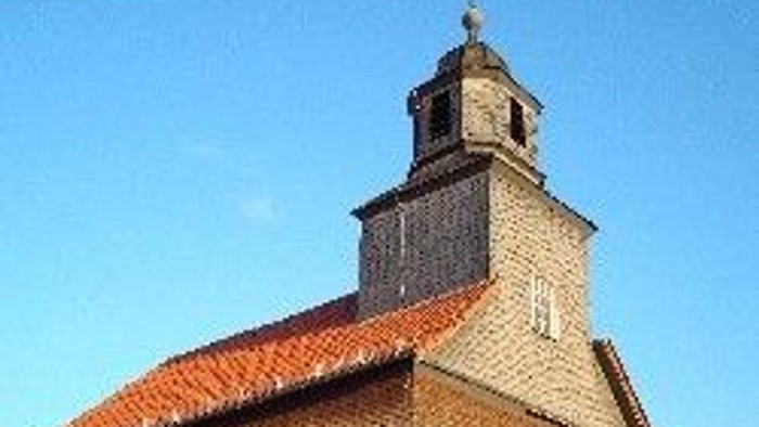 Steinkirche mit rotem Dach und hohem Glockenturm.