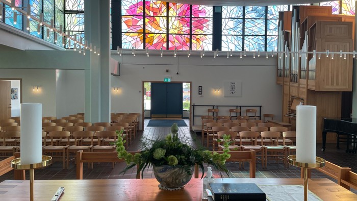 Indre del af kirke med farverige vinduesglas og træbænke.