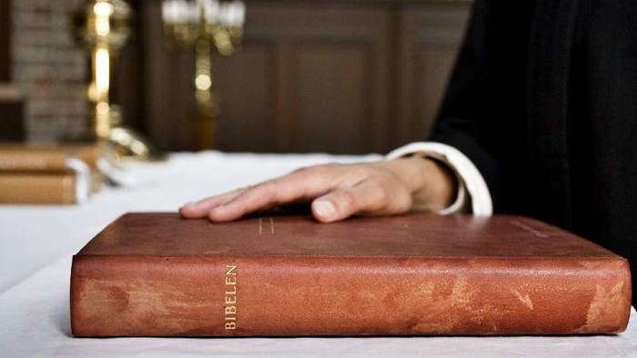 En hånd holder en gammel bibel på et bord.