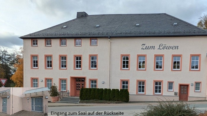 Ein großes zweigeschossiges Gebäude mit dem Schild *„Zum Löwen“*, umgeben von Grünflächen und einem bewölkten Himmel.