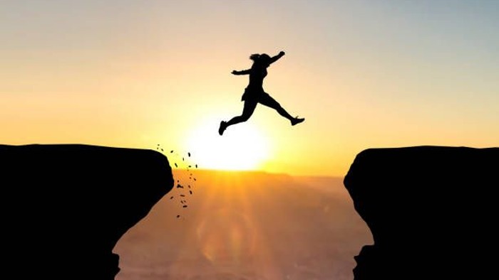 Silhouette einer Person, die bei Sonnenuntergang zwischen Klippen springt