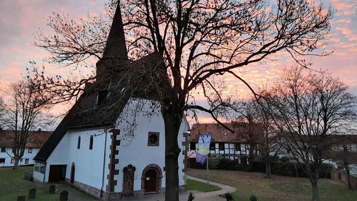 Kirche mit Turmspitze und kahlen Bäumen bei Sonnenuntergang