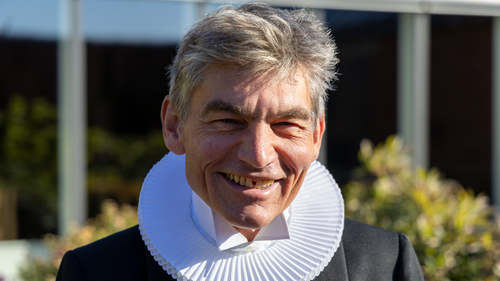 Mand med kruset krave smiler.