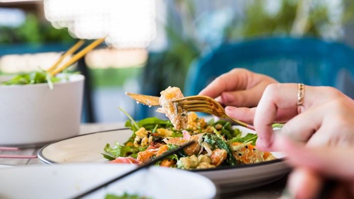 Eine Person isst ein Gericht mit Gemüse und Brot.
