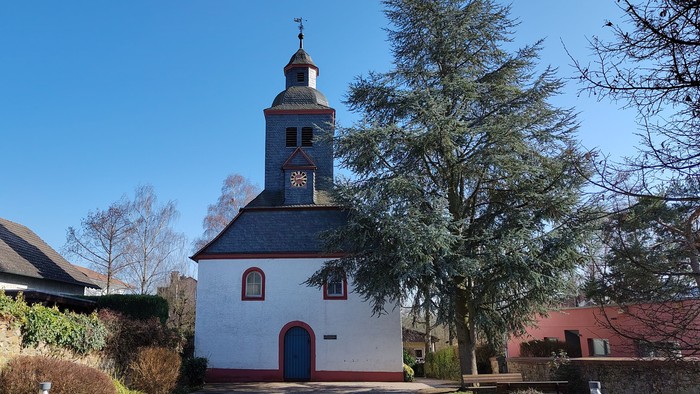Idyllische weiße Kirche mit Glockenturm in einer ruhigen, landschaftlich gestalteten Dorfgegend.