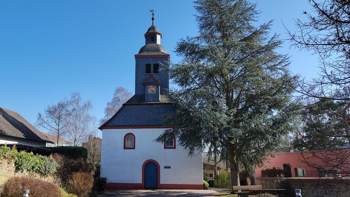 Idyllische weiße Kirche mit Glockenturm in einer ruhigen, landschaftlich gestalteten Dorfgegend.