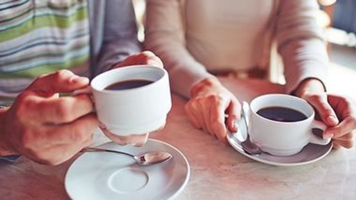 To personer holder kaffe- og teekopper på bordet.