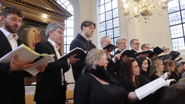 Ein Chor tritt in einer prächtigen Kirche auf und singt gemeinsam mit Notenblättern während eines formellen Konzerts.