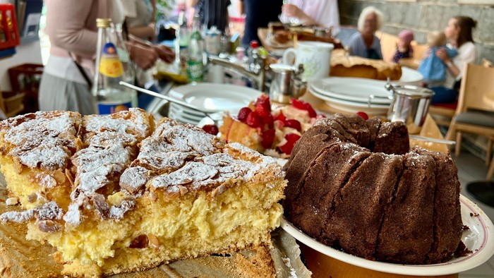 Eine köstliche Auswahl an Puderzuckerkuchen, Gugelhupf und frischem Obst auf einem rustikalen Tisch.