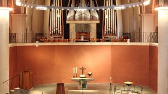 Elegante Kircheninnenausstattung mit einer großen Orgel, einem Altar und warmem Licht sowie hölzernen Kirchenbänken.