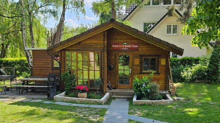 Bezaubernder Holz-Gartenpavillon mit großen Fenstern, umgeben von üppigem Grün und einer gemütlichen Sitzgruppe im Freien.