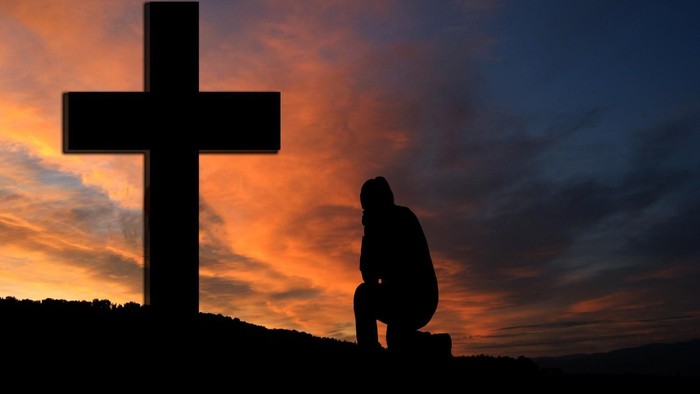 Silhouette einer Person, die bei Sonnenuntergang vor einem Kreuz kniet und betet.