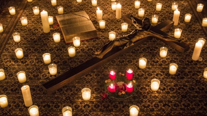 Eine feierliche Gedenkstimmung mit zahlreichen Kerzen, einem Kreuz und einem Buch auf einer gemusterten Oberfläche.
