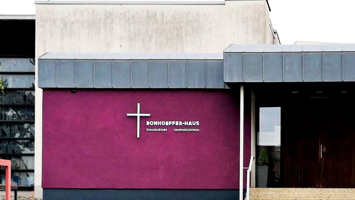Modernes Gebäude mit der Bezeichnung „Bonhoeffer-Haus“, das eine weinrote Wand und ein Kreuz-Emblem aufweist.