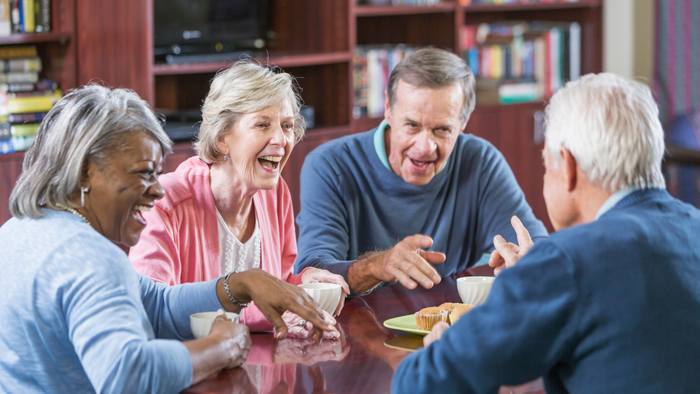 Vier Senioren genießen fröhlich ein gemeinsames Essen und Gespräch am Esstisch.