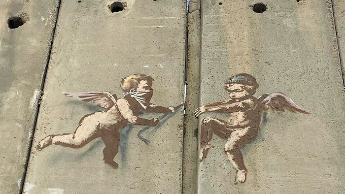 Schablonenkunst von Putten auf einer Betonsperre mit der Botschaft „Ein gerechter Frieden, nicht nur ein Stück“.