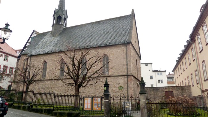 Historische Steinkirche mit hohem Turm und kahlen Bäumen in einer malerischen städtischen Umgebung.