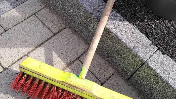 Ein Besen mit roten Borsten auf Steinplatten gelegt.
