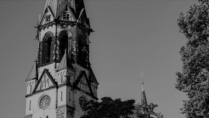 Ein hoher Kirchturm mit Uhr und spitzem Dach, daneben ein kleinerer Turm.
