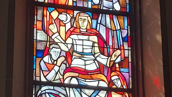Buntglasfenster mit biblischen Szenen in leuchtenden Farben und religiösen Figuren in einer Kirche.