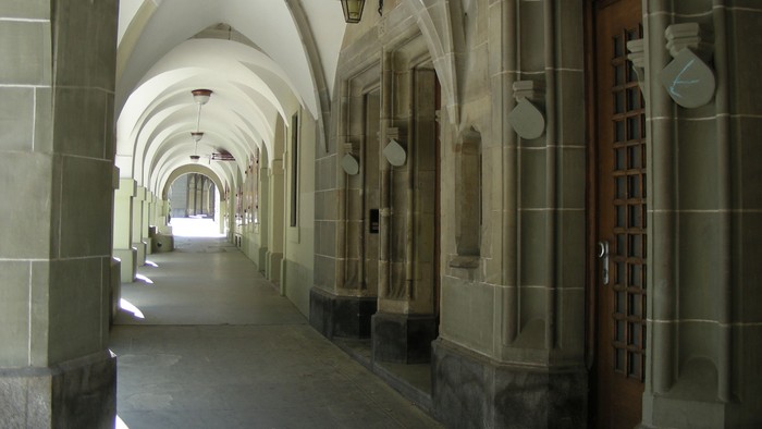 Ein langer, gewölbter Flur mit Holztüren und Wandleuchten.