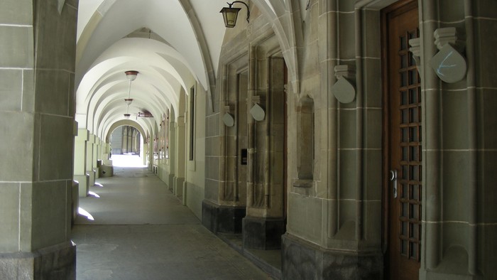 Ein langer, gewölbter Flur mit Holztüren und Wandleuchten.