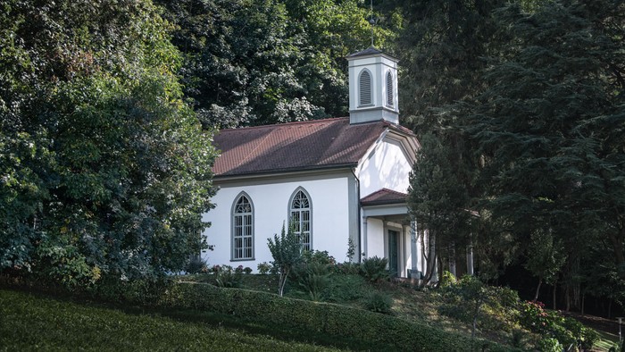 Kleine weiße Kirche mit Turm in grünem Garten.