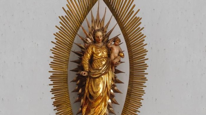 Goldene Marienstatue mit Strahlenkranz und Kerzenarrangement