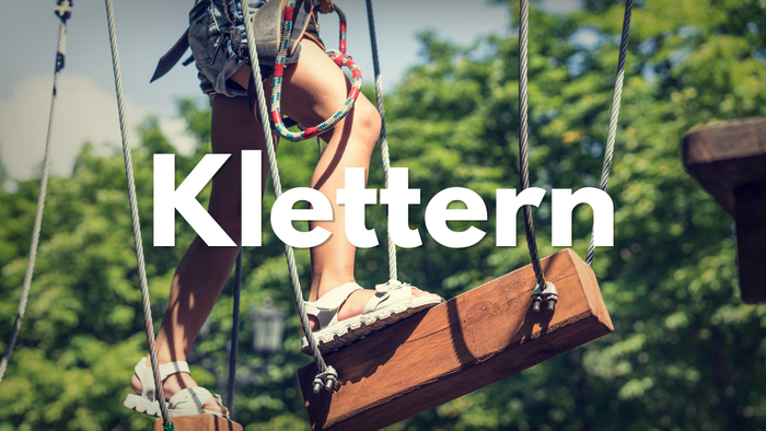 Eine Person klettert an einem hölzernen Hindernisparcours-Element mit der Aufschrift „Klettern“.