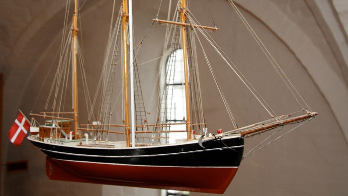 Et detaljeret modelskib med tre master, dansk flag og indviklet rigning udstillet indendørs.