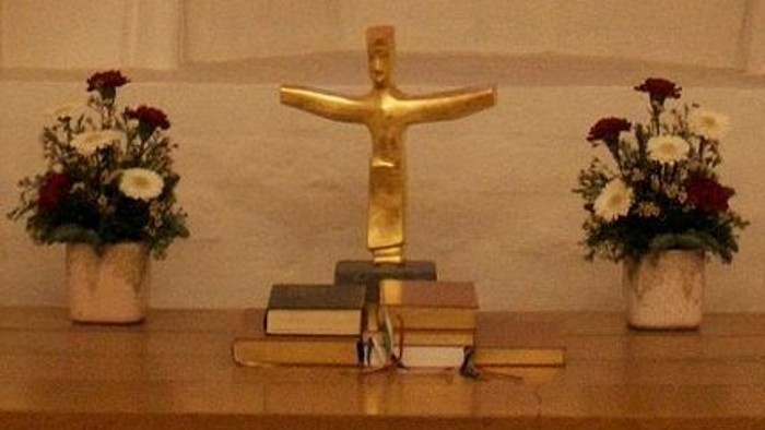 En guld farvet Jesus-statue med to blomsterstær med røde og hvide blomster på hver side.