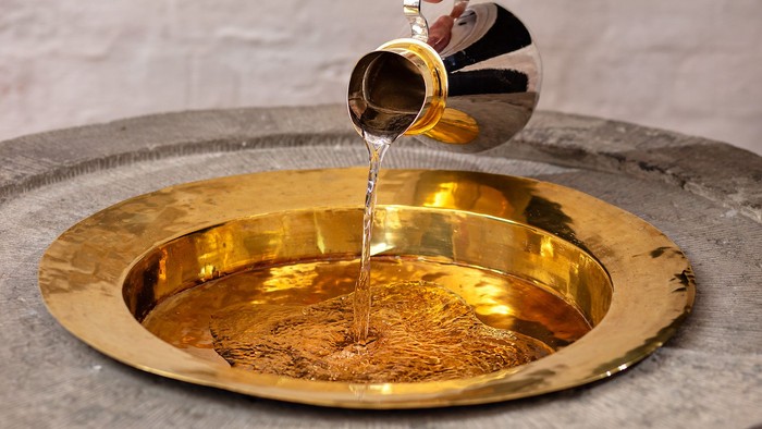 Guldskål, der fyldes med væske fra en metalkande, sandsynligvis til en rituel eller ceremoniel renselse.