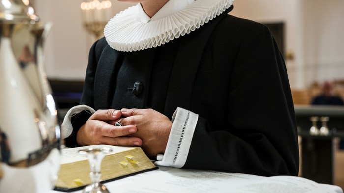 En person i traditionelt sort tøj med en krusekrave holder hænderne over en vielsesringæske.