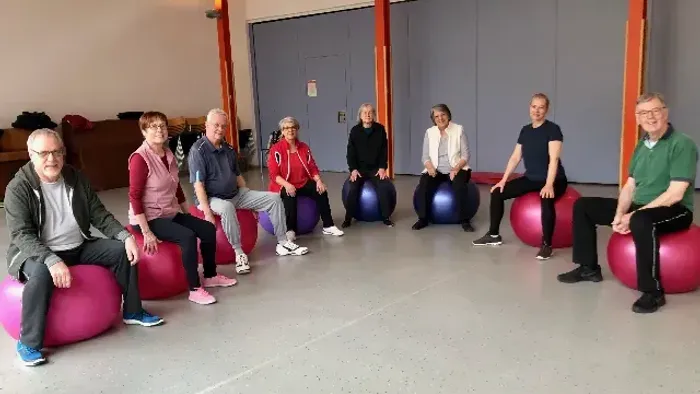 Gruppe von Menschen, die auf Gymnastikbällen in einem Raum sitzen.
