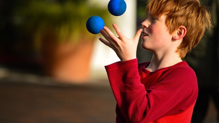 Ein Junge in rotem Pullover spielt mit zwei blauen Bällen.