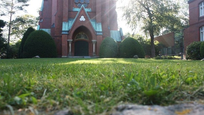 Ein Kirchengebäude mit hohem Turm und grünem Rasen im Vordergrund