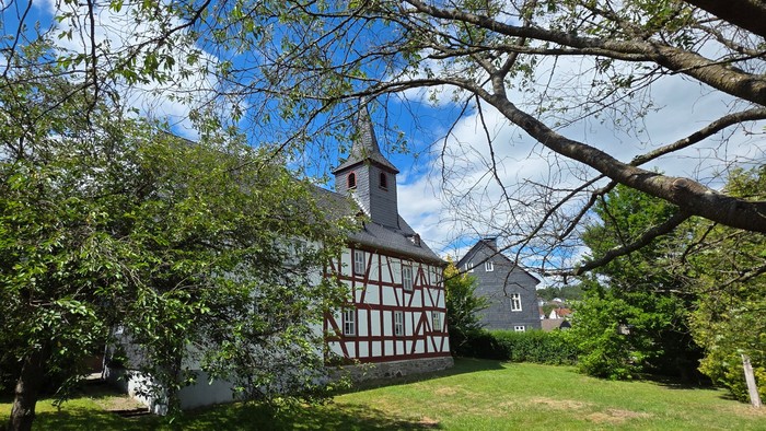 Fachwerkkirche im Hintergrund. Bäume im Vordergrund. Grüne Wiese 