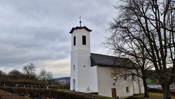 Weiße Kirche mit Turm und Uhr, umgeben von Bäumen und Himmel