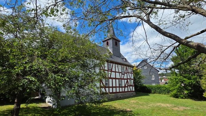 Fachwerkkirche im Hintergrund. Bäume im Vordergrund. Grüne Wiese