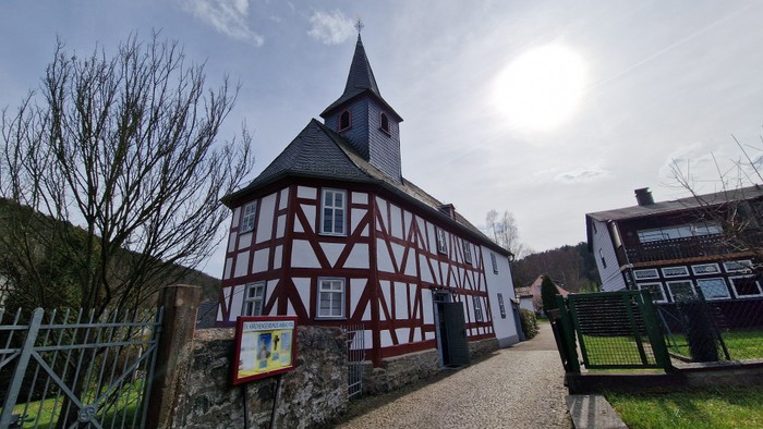 Das Bild zeigt eine traditionelle deutsche Fachwerkkirche mit einem Glockenturm und einem Weg, der zu ihr führt.