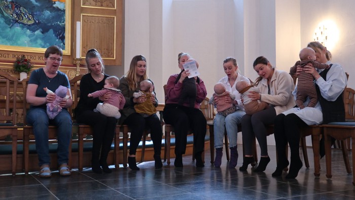 En gruppe på ni personer sidder i en kirke og holder børn i deres fætter.