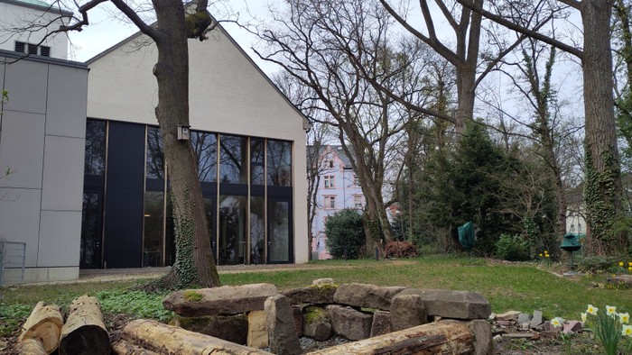 Modernes Gebäude, umgeben von einem rustikalen Holzring und kahlen Bäumen in einer Gartenlandschaft.