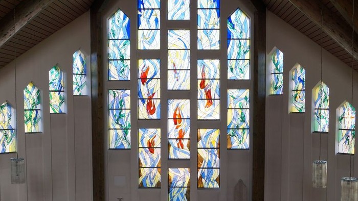 Ein ruhiges Kircheninneres mit farbenfrohen Buntglasfenstern und schlichten Holzbänken.